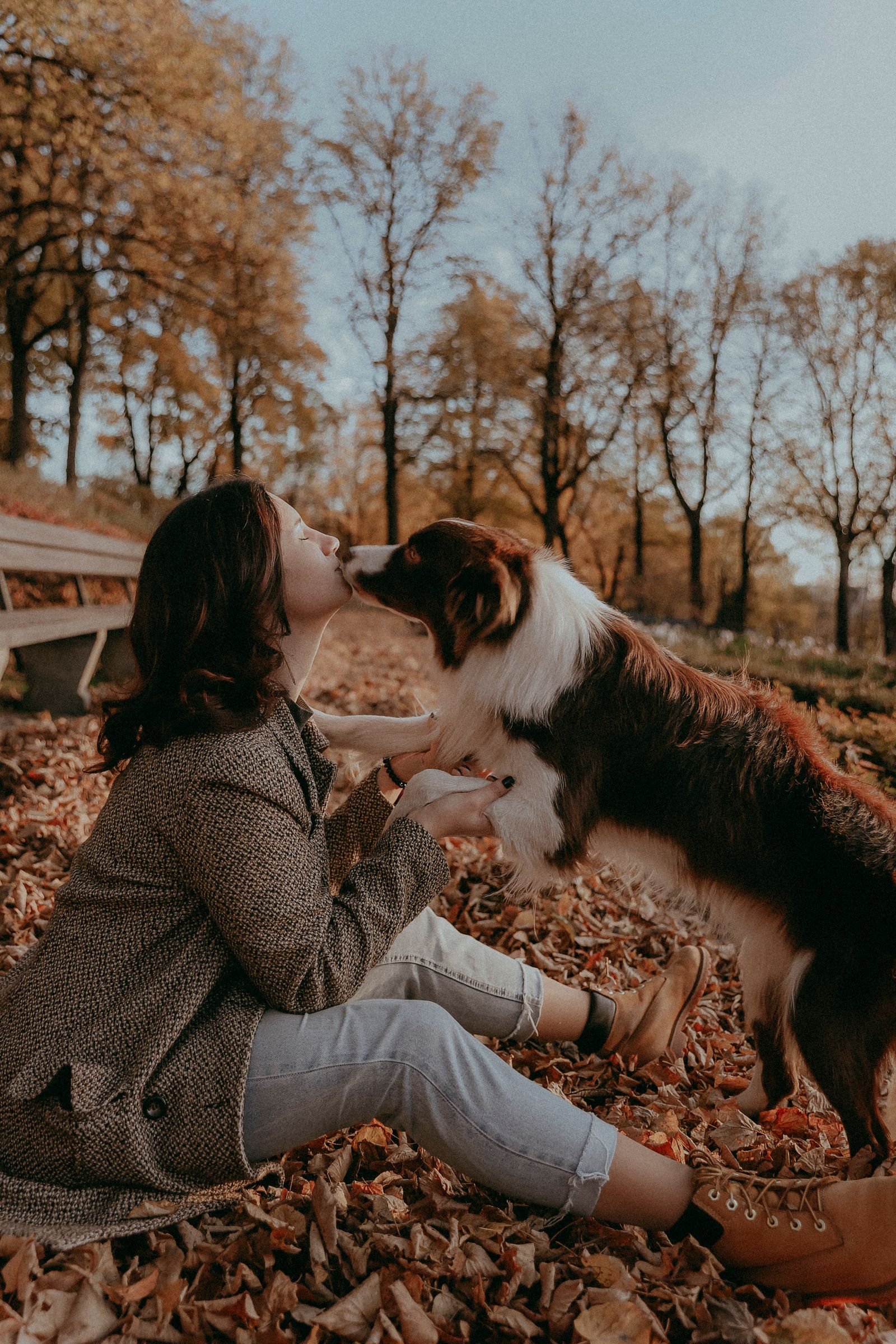 A woman leaning in as her dog licks her face in an autumn park