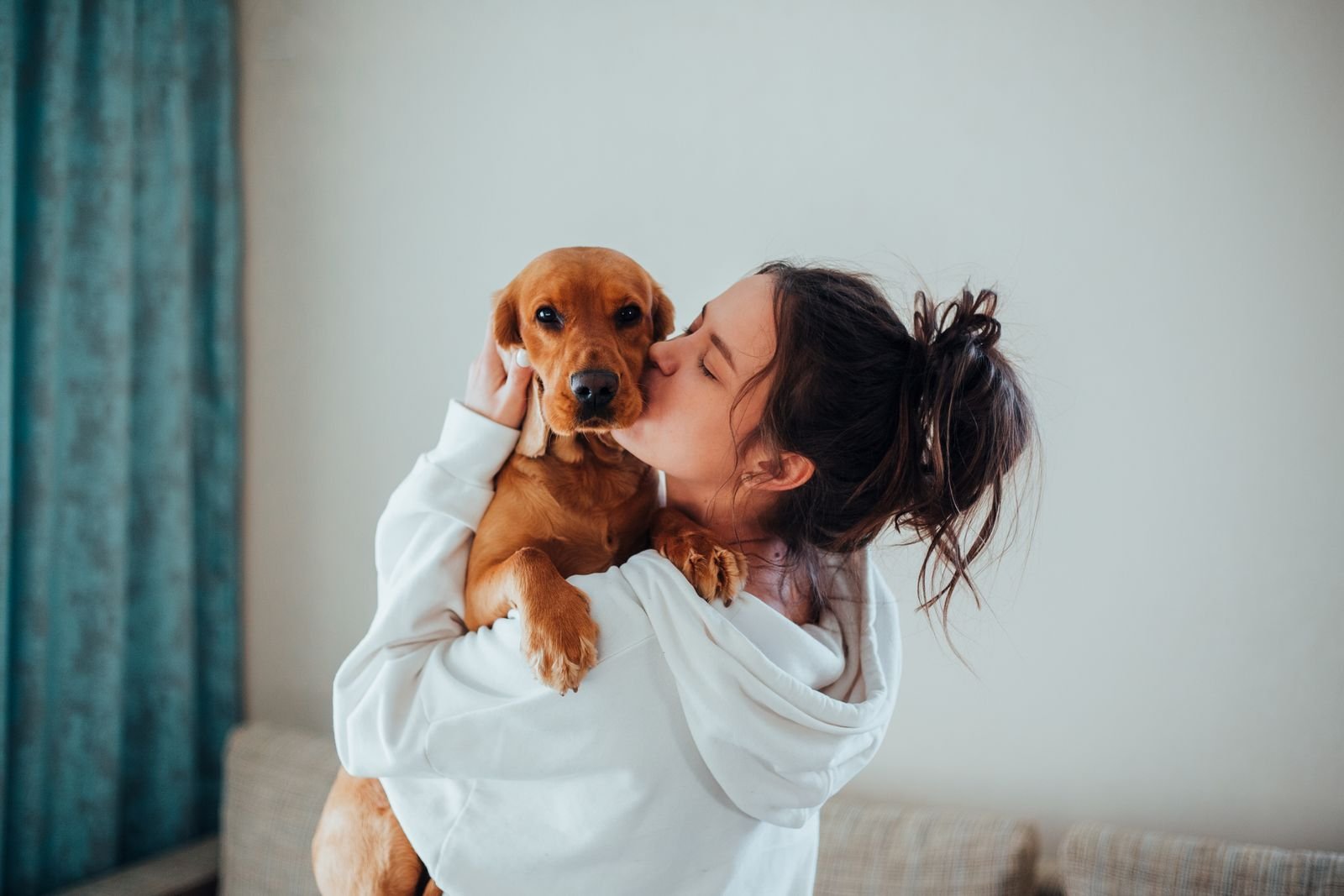 A woman kissing and cuddling her small dog indoors